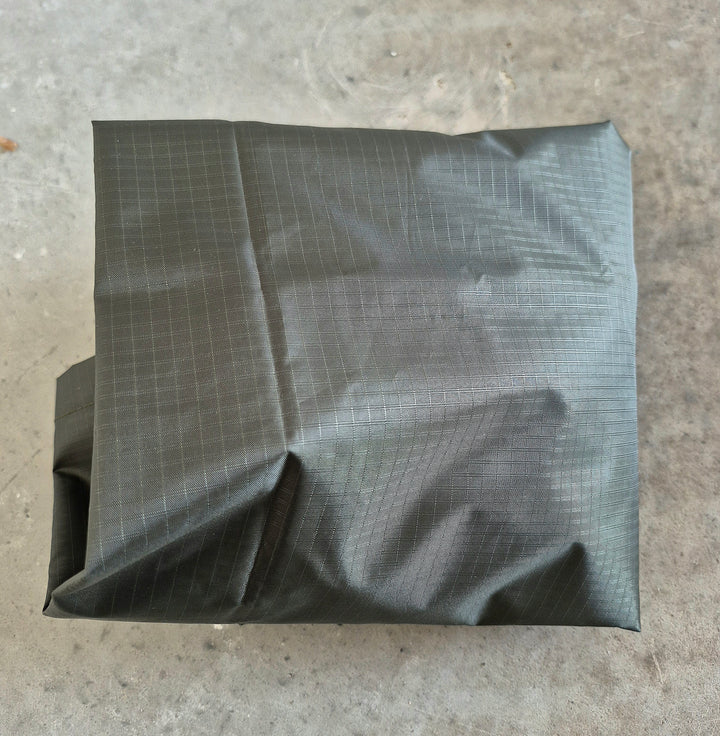 GS-009 Green Wet Weather Poncho neatly folded on concrete surface, showcasing rip-stop fabric texture and compact carry form; designed for minimalist tactical loadouts and emergency shelter packing