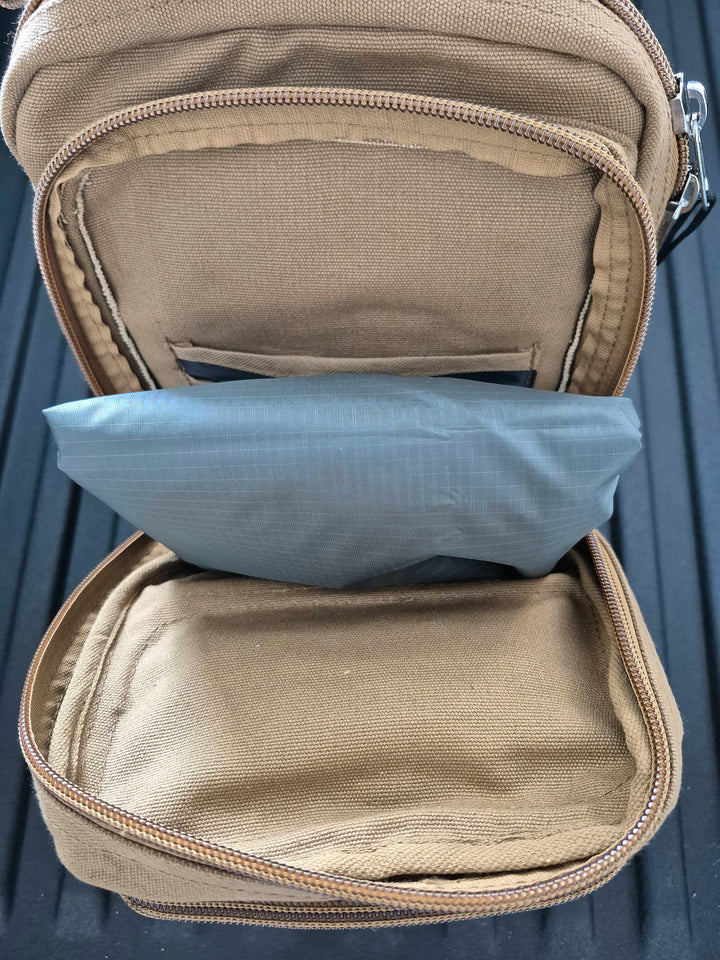 GS-009 Green Wet Weather Poncho stored inside tan tactical pack with visible blue insert pouch, placed on dark surface; illustrates compact carry configuration and modular field integration with GS-007 gear