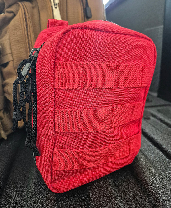 GS-010 Red Tactical Pouch displayed on black textured surface with horizontal webbing and black zipper cords; background features a brown carry bag, reinforcing rugged field gear aesthetic