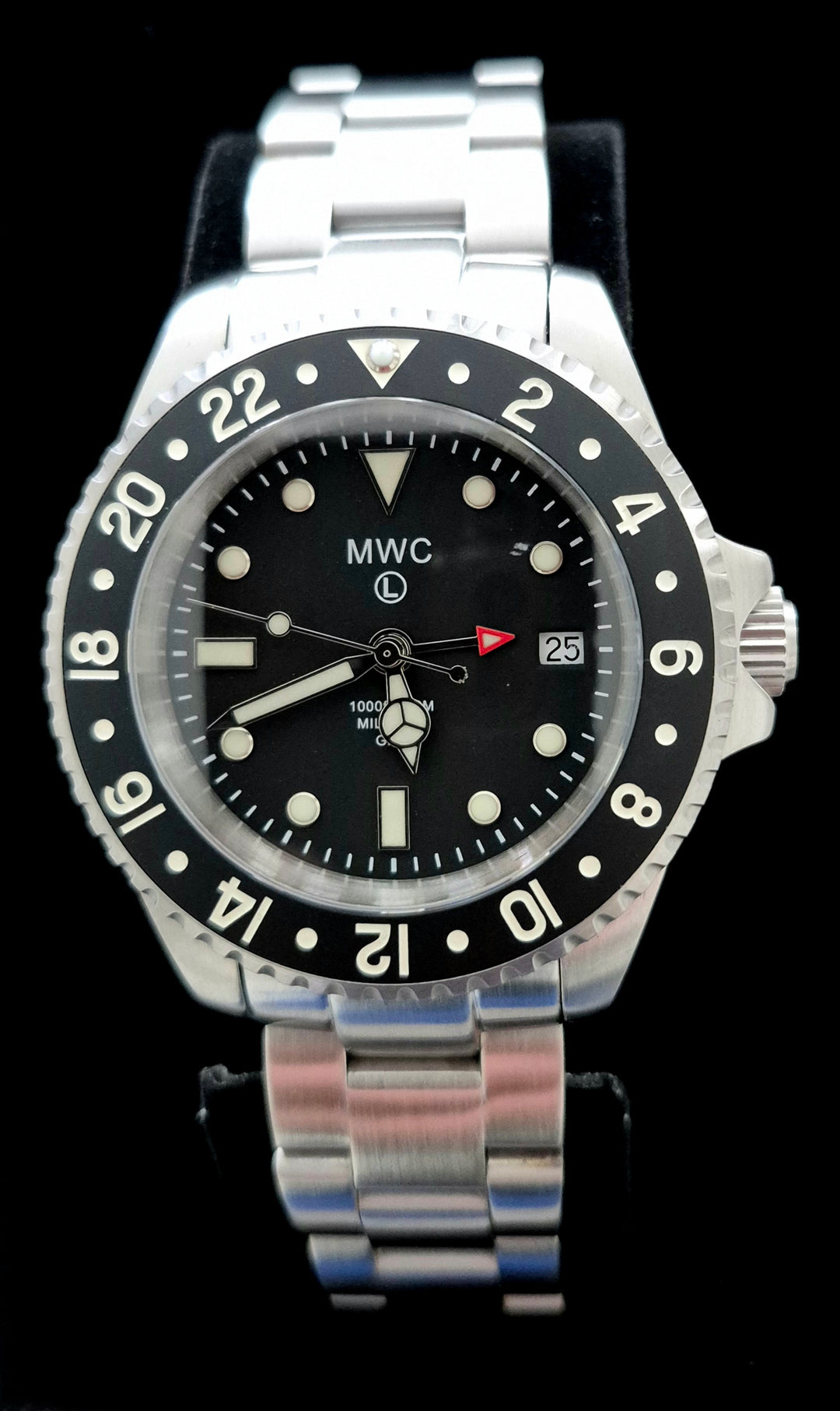 Greymont edition MWC GMT Diver Watch with black dial, red arrow-tipped 24-hour hand, and black ceramic bezel displaying numerals 2 through 22. Stainless steel bracelet with date window at 3 o’clock and “MWC 1000ft/300m” branding, set against a black background.