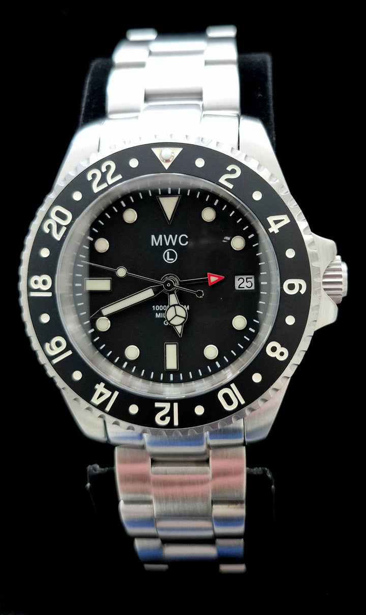 Greymont edition MWC GMT Diver Watch with black dial, red arrow-tipped 24-hour hand, and black ceramic bezel displaying numerals 2 through 22. Stainless steel bracelet with date window at 3 o’clock and “MWC 1000ft/300m” branding, set against a black background.