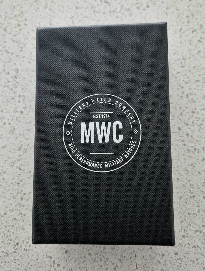 MWC military-grade watch packaging featuring EST. 1974 branding on a black box, displayed on a gray surface as part of Greymont Systems's collection.