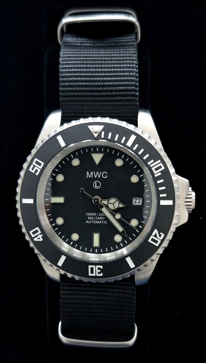 GS-001 MWC Military Automatic Watch with black dial, silver bezel, and black strap. Features date window, lumed hands, and 300m water resistance, set against a dark background for tactical product staging.