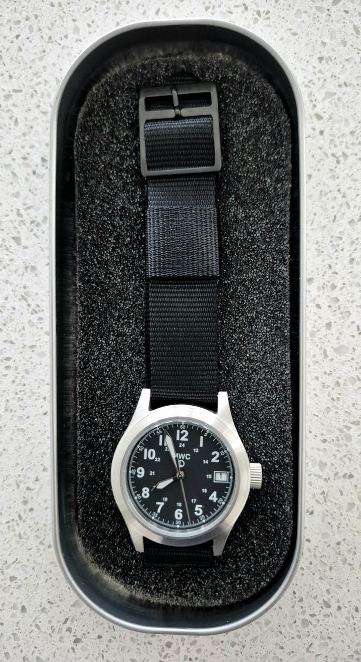 GS-002 MWC Field Watch with black dial and black strap inside a cushioned tactical watch box, displayed on a light gray surface for product staging.